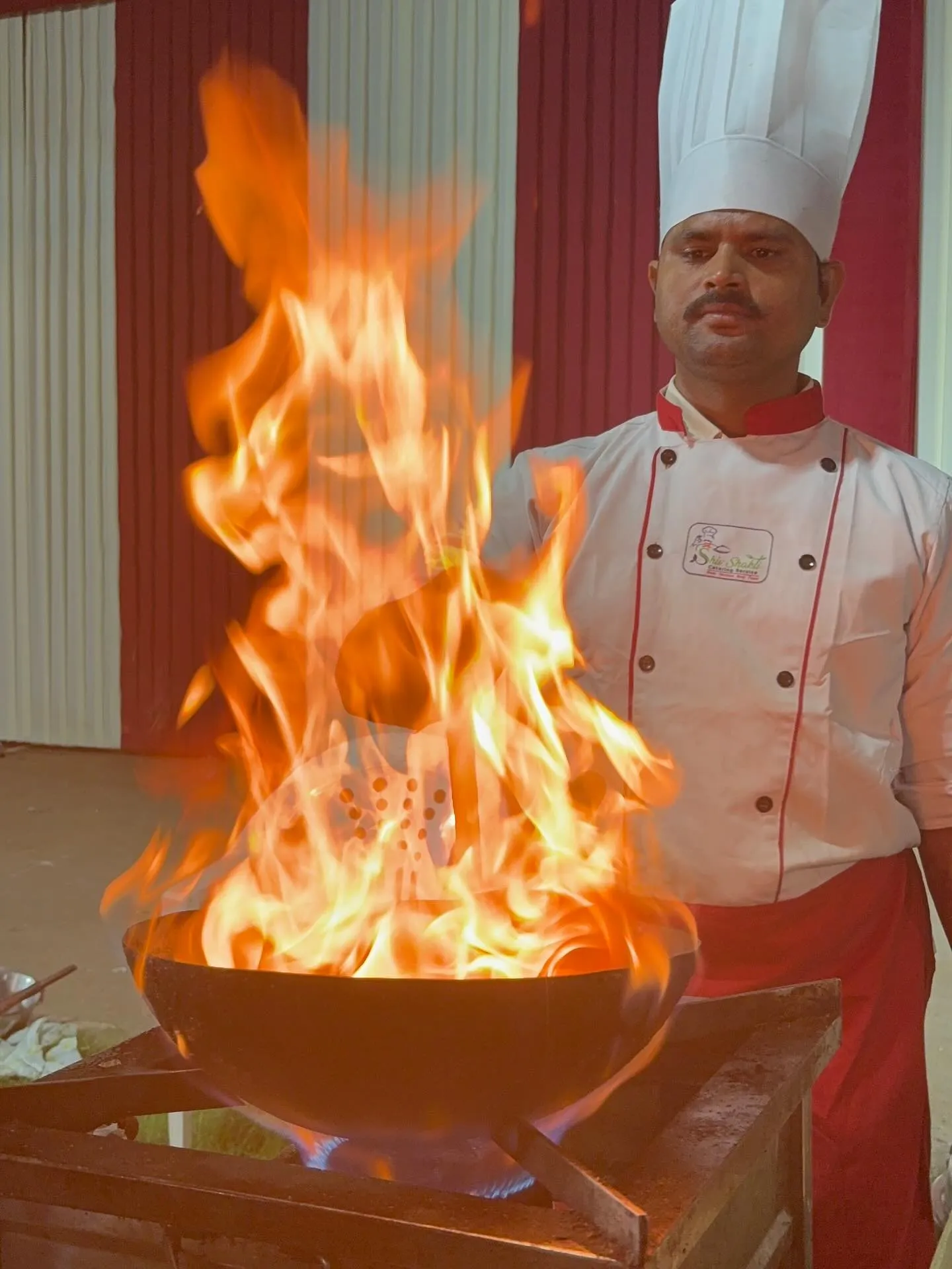Shiv Shakti chef finishing a dish tableside with a live flambé, signature of the catering house