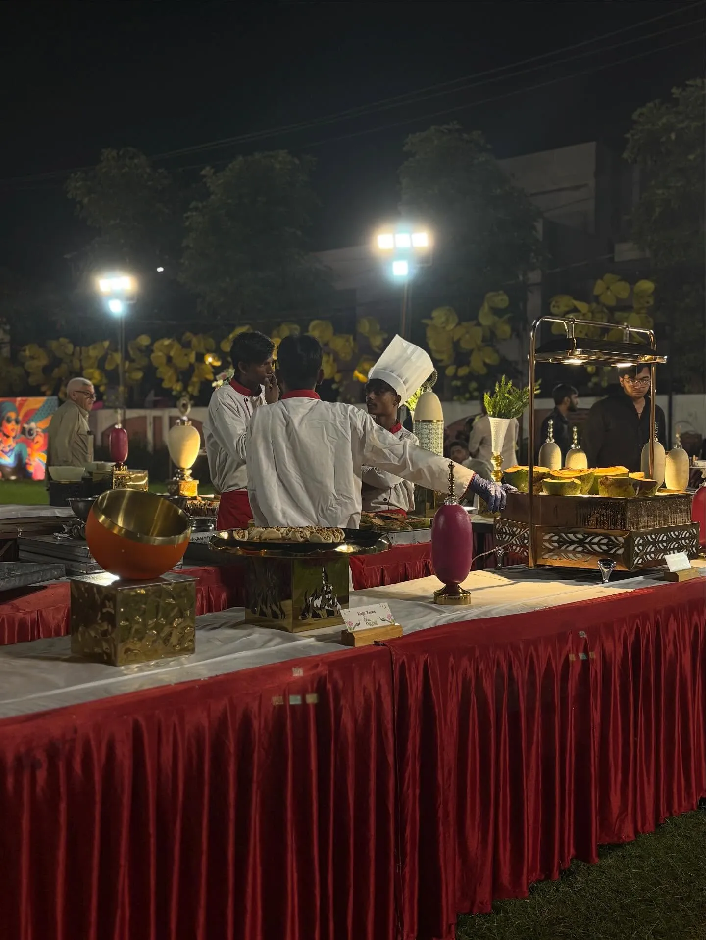Wide evening view of a Shiv Shakti catering setup with illuminated live counters